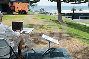 man with satellite internet dish connected working on computer at remote beach side campsite