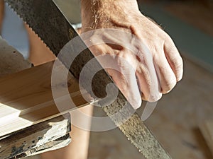 A man is sawing a board with a hand saw. Woodworking concept. Close-up