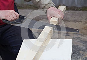 A man saws a fresh wooden board with an old rusty hand saw. Selective focus