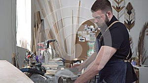 A man saws a wooden board with an electric saw in a workshop. Male craftsman works in a carpentry workshop