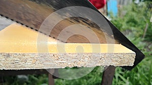 Man saws a wooden board with a hand saw