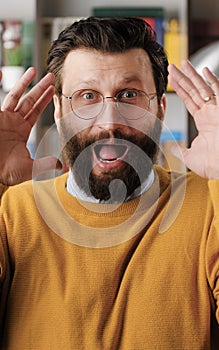 Man is scared, terrified. Frightened bearded man in glasses with suddenly throws his hands up and looking at camera, he
