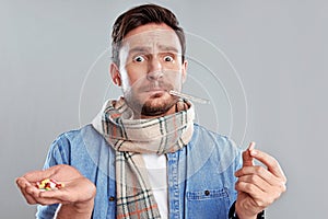 Man in a scarf holding thermometer and a hand full of pills isolated on a white background.