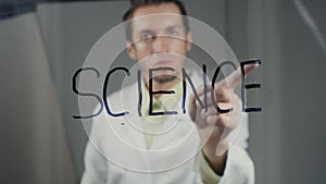 Man scientist writes the word `science` on the glass