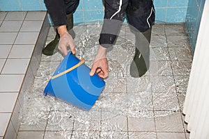 Man scoops water with a bucket from a flooded bathroom during flooding in the basement