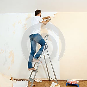 Man in with a scraper in the process of removing old wallpaper.