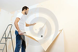 Man in with a scraper in the process of removing old wallpaper.
