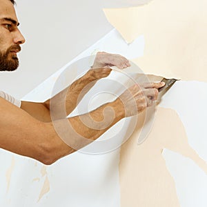 Man in with a scraper in the process of removing old wallpaper.