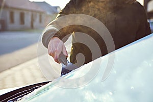 A man scrapes frost off the front window of his car on a cold morning