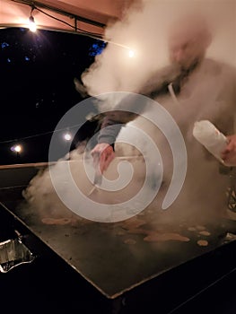 Man scrapes hot grill enveloped in rising cloud of steam