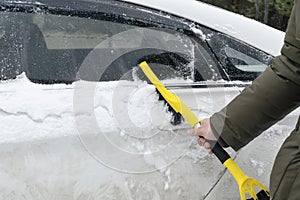 Man scraping snow from mirror car with brush. Person cleaning fresh snow after snowstorm from car in winter close up