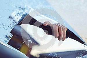 A man scratches the front window of his car on a cold winter morning