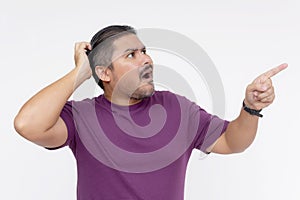 A man scratches his head looking stumped while pointing at something above and to the right. Wearing a purple waffle shirt. photo