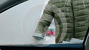 A man scratches the side window of his car on a cold winter morning