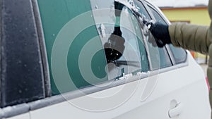 Man scratches the side window of his car on a cold winter morning