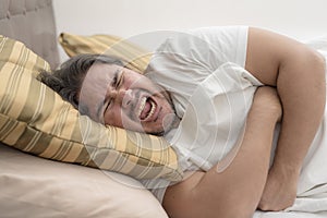 A man screams while clutching his ribcage while resting on his side on the bed. Possible pulled muscle or rib fracture