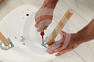 Man with screwdriver assembling stool on floor, above view