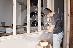 A man with a screwdriver in his hand fixes a wooden frame for a window in his house.