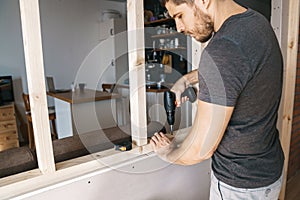 Man with a screwdriver in his hand fixes a wooden structure for a window in his house. Repair yourself.