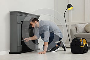 Man with screwdriver installing fireplace near wall in room