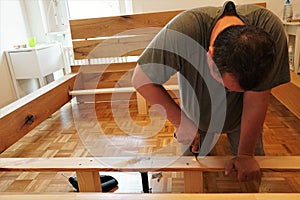 A man screwing screws in a wooden beams in assembling a new bed as improvement of his home.
