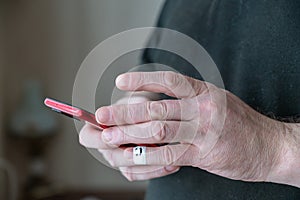 A man is scrolling through messages on his smartphone. A red smartphone is held in his hands. The first phalanx of his pinky