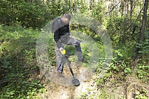 Man searches the slope in the forest in search of treasure using a metal detector.