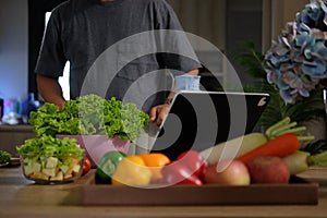 Man searching recipes on digital tablet and preparing ingredients for making healthy salad in the kitchen. Healthy lifestyle