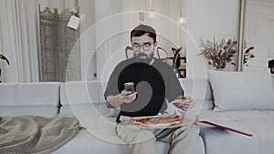 A man is seated on a comfortable couch in a house, eating pizza