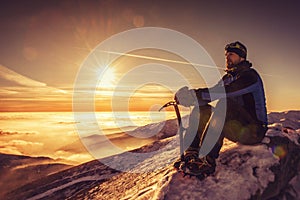 man seating on top of mountain, male hiker admiring winter scenery on a mountaintop alone with ice ax