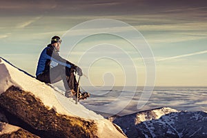 Man seating on top of mountain, male hiker admiring winter scenery on a mountaintop alone with ice ax
