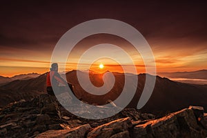 Muž sediaci na vrchole hory pri východe slnka, turistika a horolezectvo