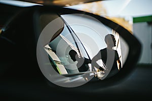 Man is seen during the side view mirror while fueling at a gas station