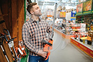 man selecting electric shears in salesroom of gardening tools shop