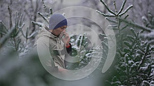 Man selects Christmas tree at Christmastime market and takes tips on correct choice by phone from his family in snowy