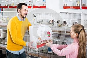 Man seller demonstrating canary bird in cage to girl in pet shop