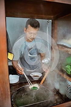 man seller draining boiled noodles with a drainer and chopsticks