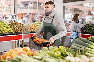 Man seller moving box of oranges in grocery shop