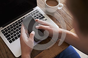 Man Sending Text Message On Mobile Phone Whilst Using Laptop