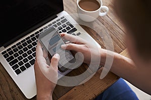 Man Sending Text Message On Mobile Phone Whilst Using Laptop