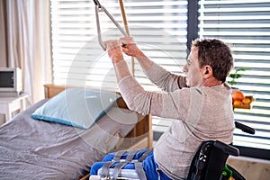 Man senior patient in wheelchair in hospital, holding onto a bed hanger.