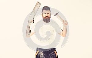 Man with serious face holds saw and hammer. Handyman concept.