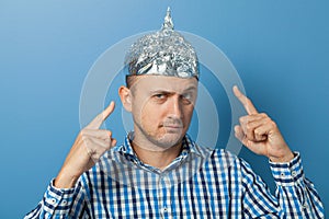 Man with a serious face shows a finger at a cap with aluminum foil. Protects from reading think