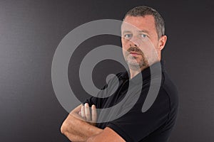 Man serious portrait in black t-shirt with arms crossed on grey background