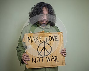 Man with serious and sad holds a cardboard poster with the inscription MAKE LOVE NOT WAR.