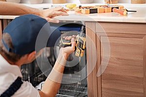 A man or a service worker in special clothes using a screwdriver attaches to the countertop or removes the dishwasher, close-up