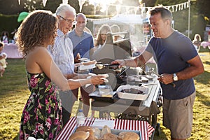 Man Serving On Barbeque Stall At Summer Garden Fete