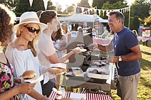 Man Serving On Barbeque Stall At Summer Garden Fete