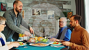 Man serving a friends with roasted chicken at multigenerational family dinner