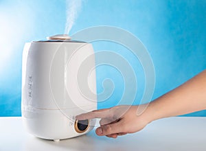 A man sets the percentage of humidity in a room on a humidifier, blue background. Copy space for text
